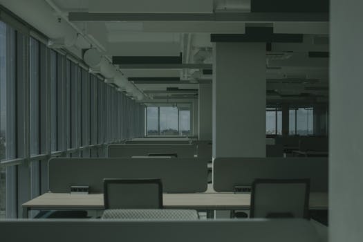 Spacious empty office with rows of desks and large windows.